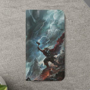 Puede incluir: Una funda de teléfono con una ilustración de Thor, el dios nórdico del trueno, empuñando su martillo. La obra de arte representa a Thor en un cielo tormentoso con relámpagos, con una capa roja y armadura. La funda es rectangular y tiene un acabado mate.