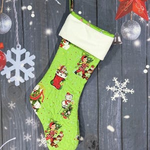 May include: A lime green quilted Christmas stocking featuring a repeating pattern of children and animals in winter attire. The stocking has a solid white plush cuff at the top and a small fabric loop for hanging. The fabric print includes red and green.
