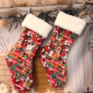 May include: Two Christmas stockings featuring a repeating Coca-Cola holiday print with Santa Claus, green pine branches, and red Coca-Cola logos. Each stocking has a white faux fur cuff at the top and a fabric loop for hanging on a wall or fireplace.