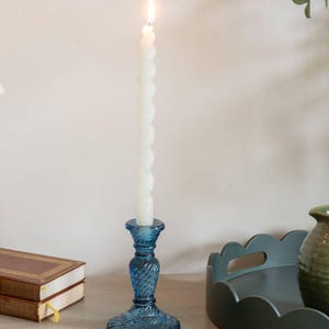 May include: A blue glass candle holder with a white candle. The candle is lit and the holder has a textured design.