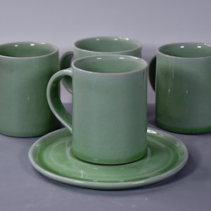 Peut inclure: Quatre tasses en céramique vertes avec des anses et une soucoupe assortie. Les tasses et la soucoupe ont une finition brillante et un effet dégradé, passant d'une nuance de vert plus claire à plus foncée.