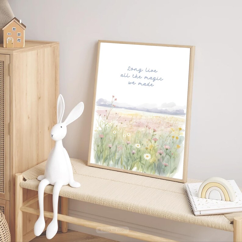 May include: A framed watercolor print with the text "Long Live all the magic we made" above a field of wildflowers. A white rabbit figurine sits on a bench next to the print. A small wooden house and a rainbow-shaped toy are also visible.
