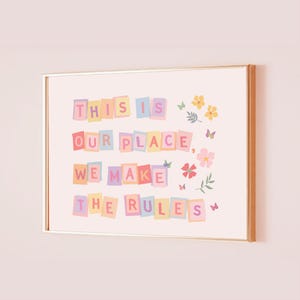May include: A framed print featuring the words "THIS IS OUR PLACE WE MAKE THE RULES" in colourful block letters. The print is decorated with floral and butterfly illustrations, set against a pale pink background.