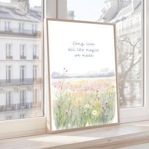 May include: A framed watercolor print featuring a field of wildflowers in soft pinks, yellows, and greens. The artwork includes the text "Long live all the magic we made" in a delicate blue script. The frame is a light wood color.
