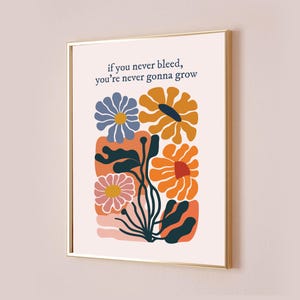May include: A white framed print with a quote about growth and a colorful floral illustration. The quote reads "if you never bleed, you're never gonna grow". The flowers are orange, yellow, blue, and pink.