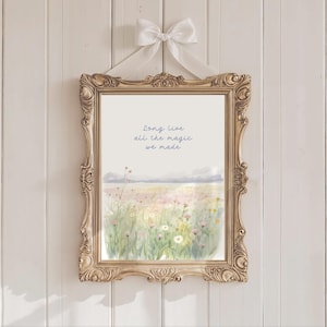 May include: A framed print with a watercolor landscape of a field of wildflowers, mountains, and the text "Long Live all the magic we made." The ornate gold frame is suspended by a white ribbon tied in a bow.