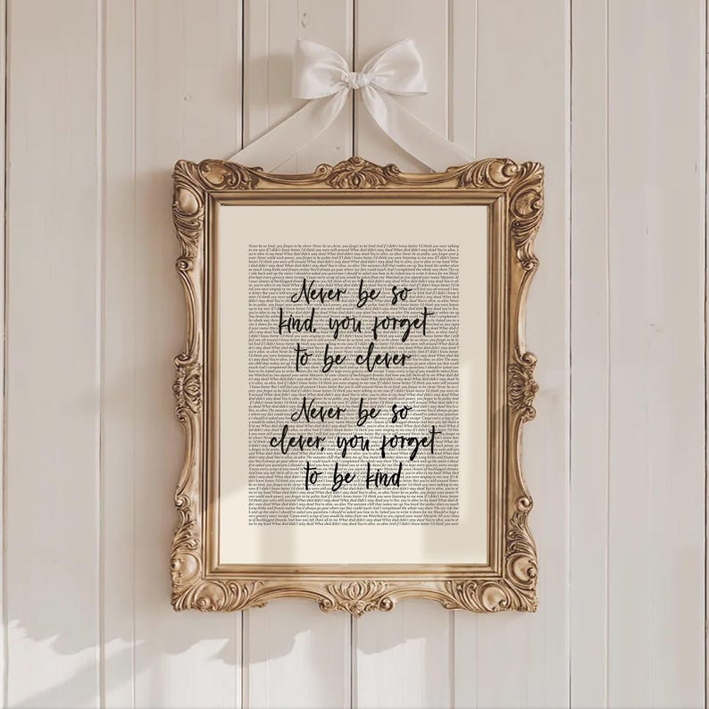 May include: A framed print with a gold ornate frame and a white ribbon. The print features the text "Never be so kind, you forget to be clever. Never be so clever, you forget to be kind" in black script over a background of smaller text.