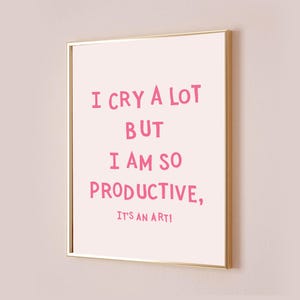 May include: A framed print with a gold border and a light pink background. The text in pink reads: "I CRY A LOT BUT I AM SO PRODUCTIVE, IT'S AN ART!"