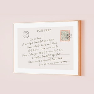 May include: A framed postcard print with a gold border. The postcard has a beige background with handwritten text and a postage stamp. The text includes phrases like "We lie back" and "Like when we were young."