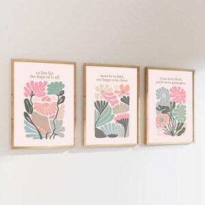 Puede incluir: Tres impresiones artísticas enmarcadas con diseños florales y citas inspiradoras. Las impresiones presentan colores pastel, incluyendo rosa, verde y melocotón, con texto que dice "to live for the hope of it all", "never be so kind, you forget to be clever", y "if you never bleed, you're never gonna grow".