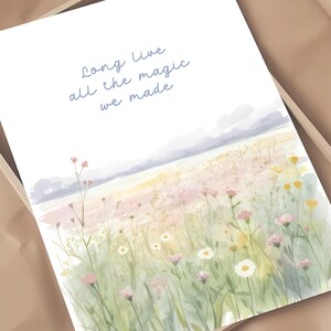 May include: A watercolor print featuring a field of wildflowers in shades of pink, yellow, and white, with a soft, pastel-colored sky. The text "Long live all the magic we made" is written in light blue script.