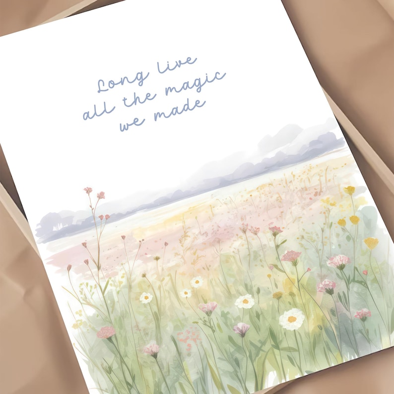 May include: A watercolor print featuring a field of wildflowers in shades of pink, yellow, and white, with a soft, pastel-colored sky. The text "Long live all the magic we made" is written in light blue script.