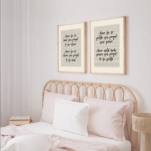 May include: Two framed prints with inspirational quotes in black script. The prints are in light wood frames and hang above a bed with pink bedding. The quotes include phrases like "Never be so kind you forget to be clever."