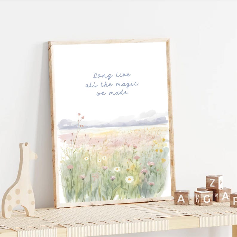 May include: A framed watercolor print featuring a field of wildflowers in pastel colors. The artwork includes the text "Long Live all the magic we made" in light blue script. The frame is a light wood color.