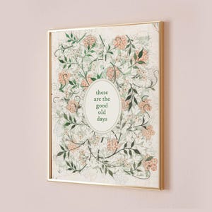 May include: A framed print with a gold-colored frame. The artwork features a floral pattern in shades of green, white, and peach. An oval in the center contains the text "these are the good old days".