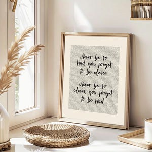 May include: A framed print with the text "Never be so kind, you forget to be clever. Never be so clever, you forget to be kind" in black script. The background is a light beige colour, and the frame is gold.
