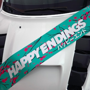 May include: A teal banner with the words "HAPPY ENDINGS" in white, accented with pink cherry blossoms and Japanese text. The banner is placed diagonally across a white car hood.