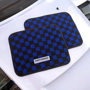 May include: Two car floor mats with a blue and black chequered pattern. The mats have a black border and a white label that reads "HAPPY ENDINGS". The mats are rectangular and sit on a white surface.