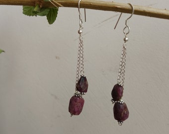 May include: A pair of silver dangle earrings with two dark pink, faceted gemstone beads on each earring.