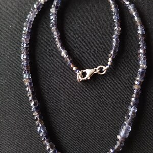 May include: A necklace made of small, faceted, dark blue gemstones. The necklace is strung on a silver chain and has a silver clasp.