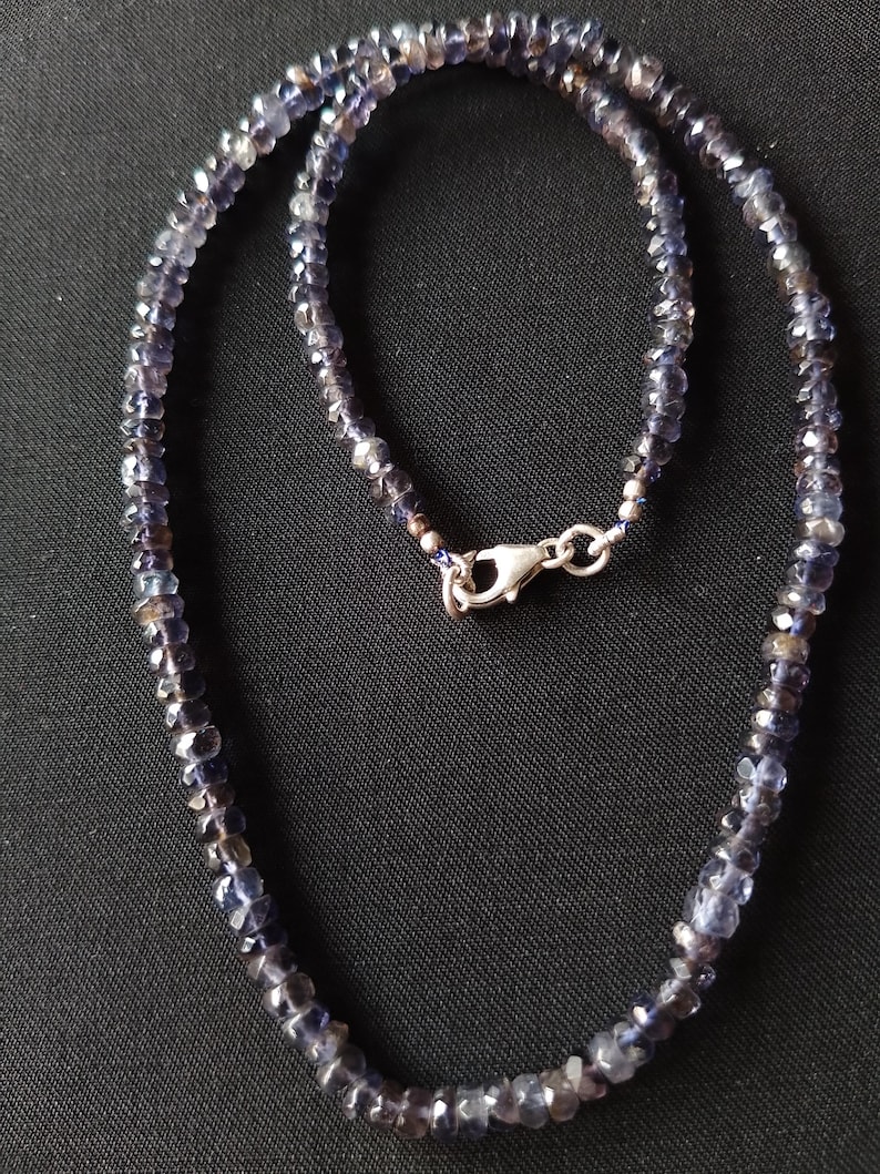May include: A necklace made of small, faceted, dark blue gemstones. The necklace is strung on a silver chain and has a silver clasp.