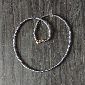 May include: A silver necklace with small, light blue beads. The necklace is on a dark wood surface.