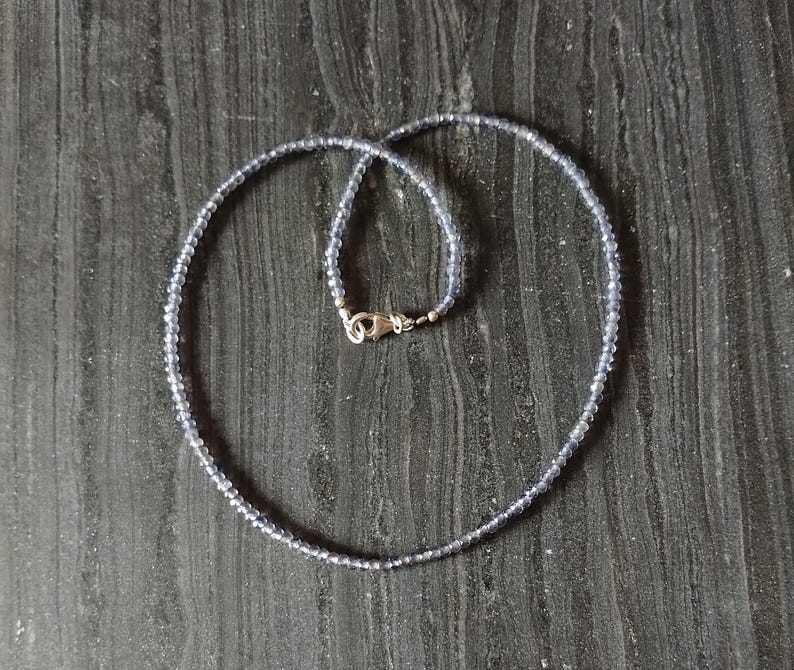 May include: A silver necklace with small, light blue beads. The necklace is on a dark wood surface.