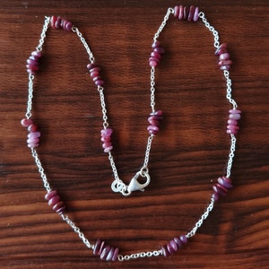 May include: A silver chain necklace with small, flat, pink and purple gemstone beads.