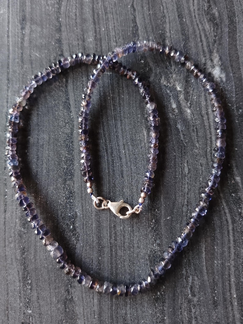 May include: A necklace made of small, faceted, dark purple gemstones. The necklace is strung on a silver chain and has a silver clasp.