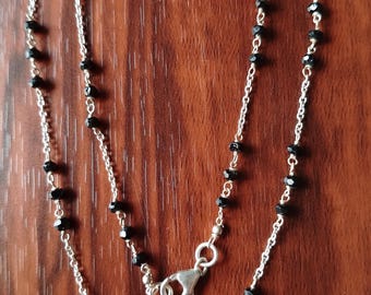 May include: A silver chain necklace with black beads. The necklace has a lobster clasp closure.