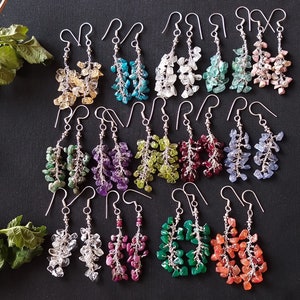 Könnte beinhalten: Ein Set mit 12 Paaren Hängeohrringen mit verschiedenen Edelsteinfarben, darunter Grün, Blau, Lila, Rot, Orange und Klar. Jeder Ohrring ist aus Silberdraht gefertigt und hat einen Cluster aus kleinen, unregelmäßig geformten Edelsteinen.