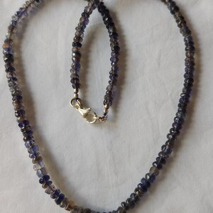 May include: A necklace made of small, faceted, dark blue gemstones. The necklace is strung on a silver chain and has a silver clasp.