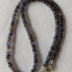 May include: A necklace made of dark blue and grey faceted gemstone beads. The necklace has a silver clasp.