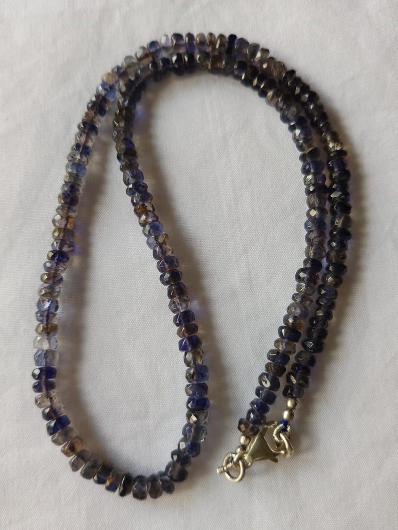May include: A necklace made of dark blue and grey faceted gemstone beads. The necklace has a silver clasp.