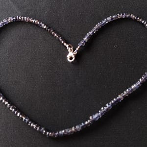 May include: A silver necklace with a heart-shaped chain made of small, dark blue gemstones.