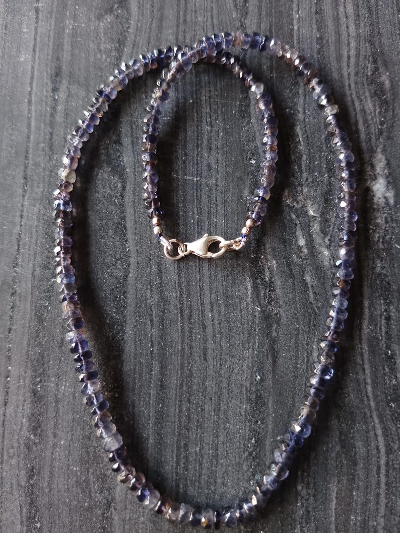 May include: A silver necklace with a clasp fastening, made with small, faceted, dark purple gemstones.