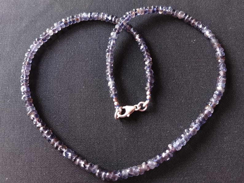 May include: A silver chain necklace with small, dark blue gemstone beads.