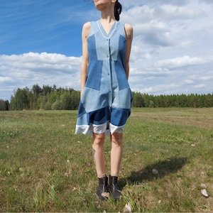 Può includere: Un abito in denim blu con un design a patchwork. L'abito ha una chiusura con bottoni sul davanti ed è senza maniche.