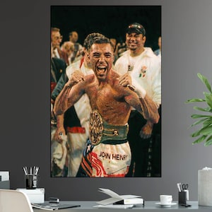 May include: A framed print of a boxer celebrating a victory. The boxer, shirtless, wears a championship belt and boxing shorts with the name "JOHN HENRY" visible. The image captures the boxer's expression of joy and triumph.
