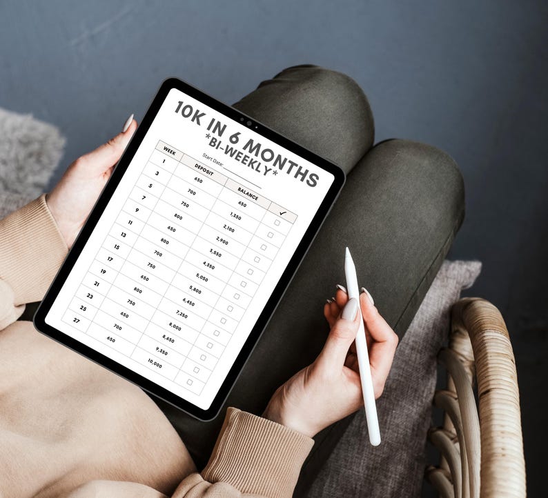 May include: A digital tablet displaying a spreadsheet with the title "10K in 6 Months *Bi-Weekly*" and a column for "Deposit" and "Balance". The spreadsheet shows a plan to save $10,000 in six months by making bi-weekly deposits.