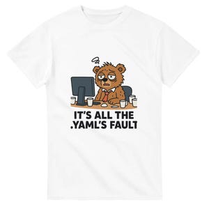May include: A white short-sleeved t-shirt featuring a graphic of a tired brown bear sitting at a desk with a computer and multiple coffee cups. Below the bear, the text reads IT'S ALL THE .YAML'S FAULT in bold black capital letters.