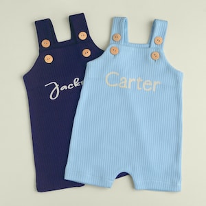 May include: Two personalized baby onesies, one navy blue with the name "Jack" embroidered on it and one light blue with the name "Carter" embroidered on it.