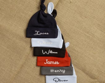 May include: A stack of six baby hats with different names embroidered on them. The hats are blue, light blue, black, red, gray, and light blue. The names are Lucas, Oliver, William, James, Henry, and Oliver.
