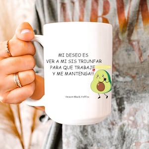 May include: White ceramic mug with a black handle. The mug has a graphic of an avocado with a halo and a heart. The text on the mug reads "MI DESEO ES VER A MI SIS TRIUNFAR PARA QUE TRABAJE Y ME MANTENGA!!!" and "Desert Black Coffee".