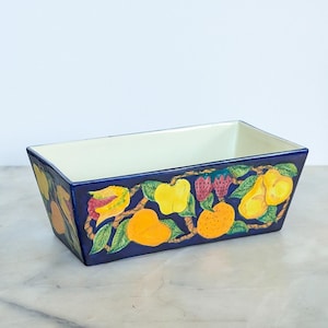May include: A rectangular ceramic planter with a deep blue exterior featuring a hand-painted pattern of yellow and orange fruits, including pears and citrus, with green leaves and brown stems. The interior of the vessel is a solid off-white color.