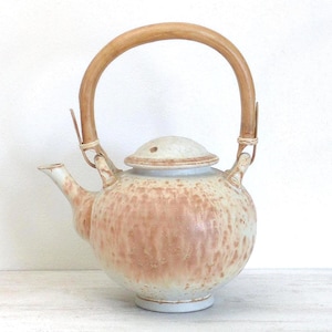 May include: A ceramic teapot with a light brown and peach speckled glaze. It features a bamboo handle and a matching lid. The spout and base are white. This teapot is a decorative kitchenware item.