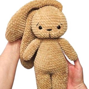 Op de afbeelding: Een bruin gehaakt pluche konijn speelgoed met zwarte ogen en een lang slap oor. Het konijn staat op zijn eigen twee voeten.