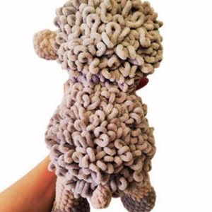 May include: A handmade, plush sheep toy in shades of gray. The sheep has a curly, textured body, small ears, and four stubby legs. The toy is held by a person's hand against a white background. The sheep is approximately 8 inches tall.