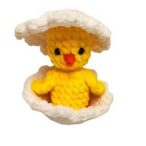 May include: A small, yellow, crocheted chick figure emerging from a white, textured, crocheted eggshell. The chick has two black bead eyes and a small, bright orange, crocheted beak. The eggshell is split into two halves, with one piece on top.