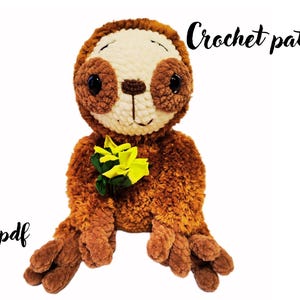 Könnte beinhalten: Ein braunes Faultier-Plüschtier mit cremefarbenem Gesicht, dunkelbraunen Augenpartien und schwarzen Sicherheitsaugen. Das Faultier hält einen kleinen Strauß leuchtend gelber Blumen. Der Text "Crochet pattern" und "eng / pdf" ist in schwarzer Schrift.